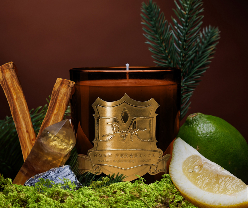 Candle with decorative emblem surrounded by cinnamon sticks, a lime, and lemon on a dark background