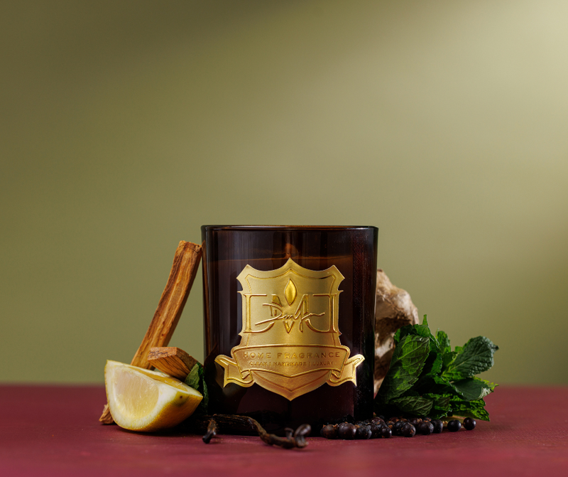 Decorative candle with a gold emblem on a red surface with greenery and a lemon slice.