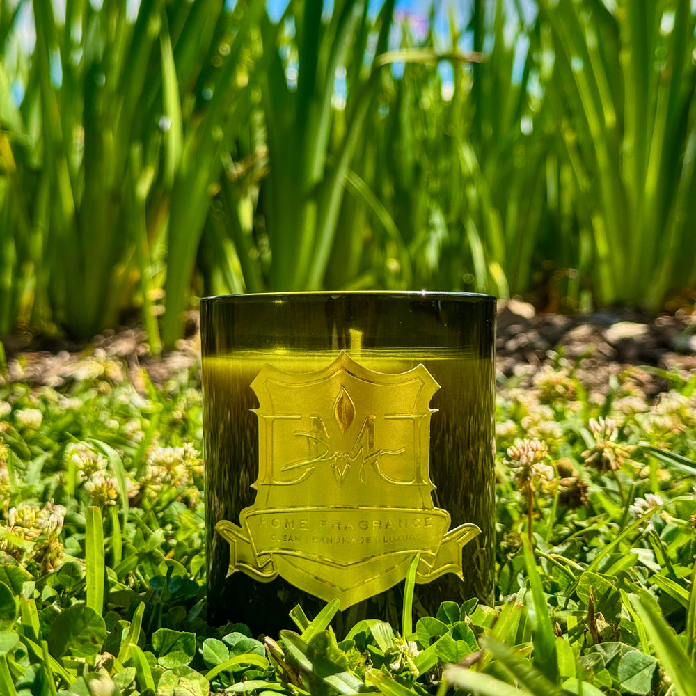 Roots candle by DMJ Home Fragrance in green vessel placed in grass outdoors inspired by Louisiana nature and Moncus Park