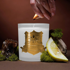 A hand lighting a candle with a gold label design, surrounded by lemon zest and oakmoss. DMJ Home Fragrance candle. Luxury Clean Candle.