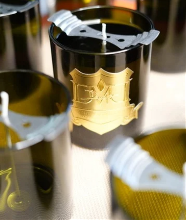 Custom branded candle produced by DMJ Home Fragrance featuring a gold crest logo on an amber glass vessel during private label candle production