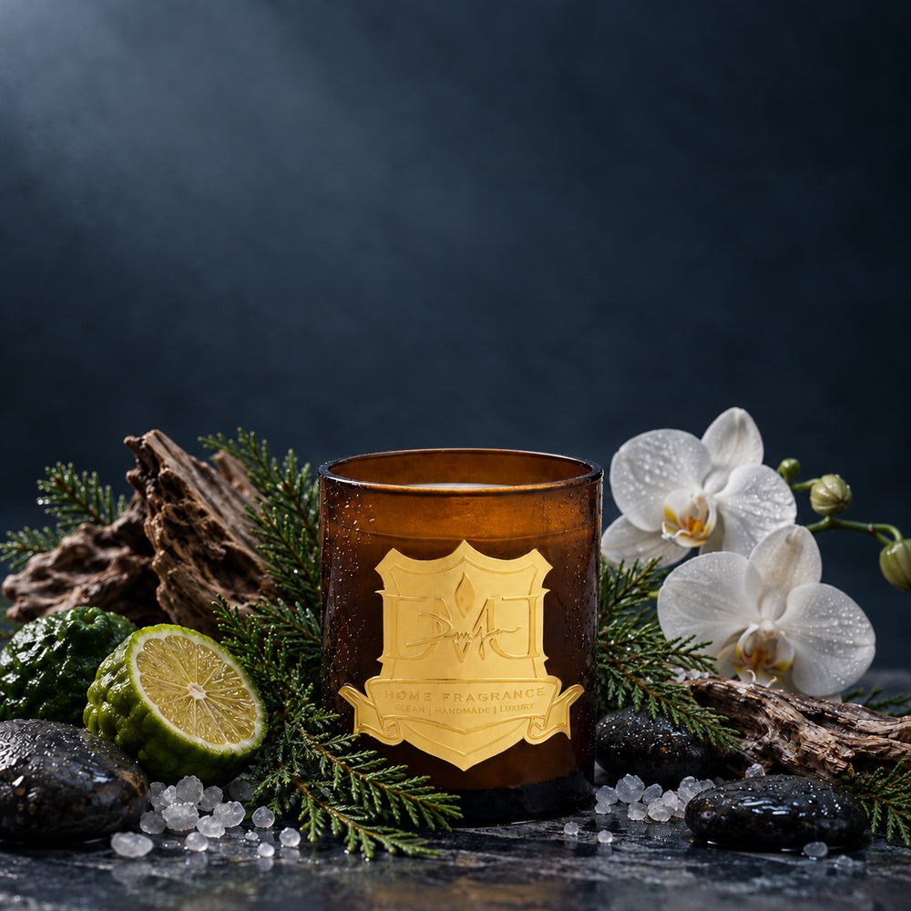 Water Wood Candle by DMJ Home Fragrance in amber glass with a gold crest label, styled with white orchids, halved bergamot, cedar, driftwood, sea salt and wet stones on a slate blue backdrop
